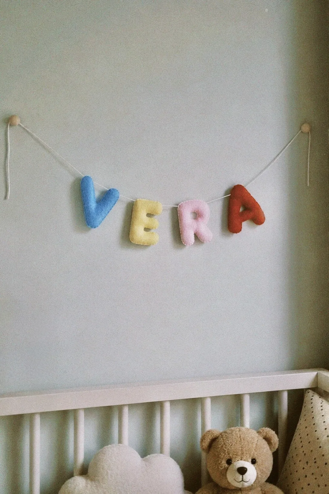 Vilten naamslinger met de naam Vera boven een wit babybedje